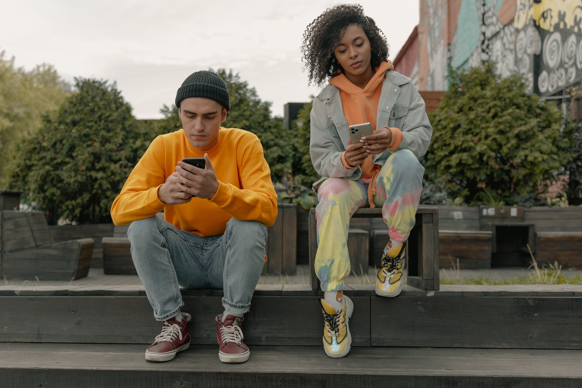 a man and a woman siting on a wooden platform holding smartphones