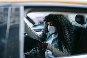 focused black woman in medical mask browsing smartphone in car