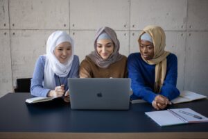 cheerful diverse muslim women browsing laptop in classroom