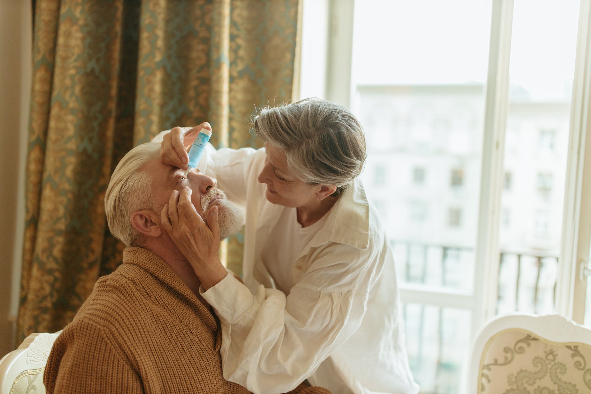 elderly woman putting eyedrops into the eyes of an elderly man