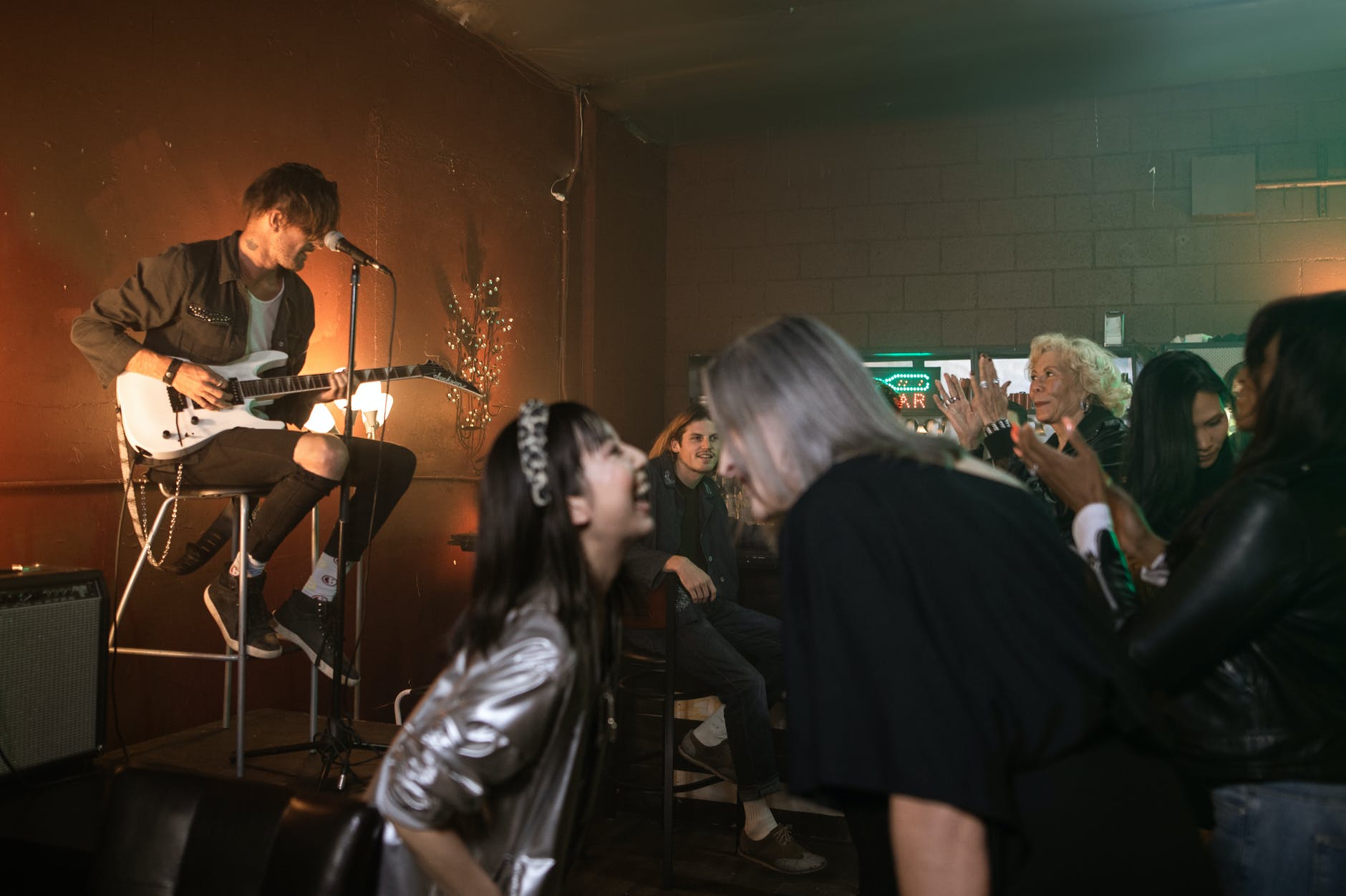 women dancing while a man in black t shirt is playing guitar