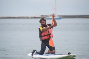 a man wearing a life vest kneeling on a sup board paddling