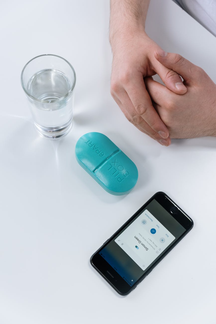 drinking glass beside blue plastic pill box and mobile phone