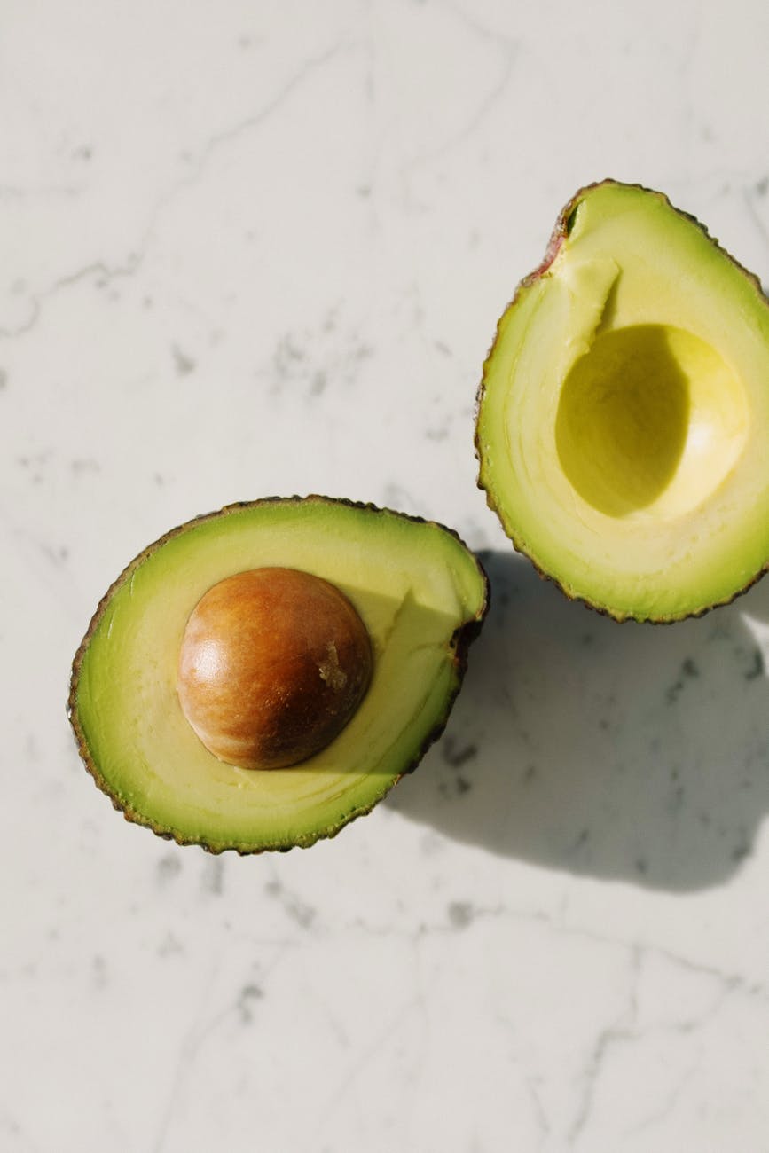 halves of fresh green avocado on marble surface