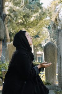 ethnic woman in traditional outfit praying on cemetery