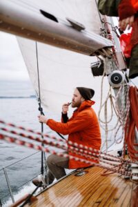 man in orange jacket holding a tabaco pipe while sitting on the boat