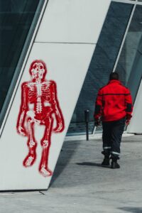 man walking past graffiti of skeleton on wall
