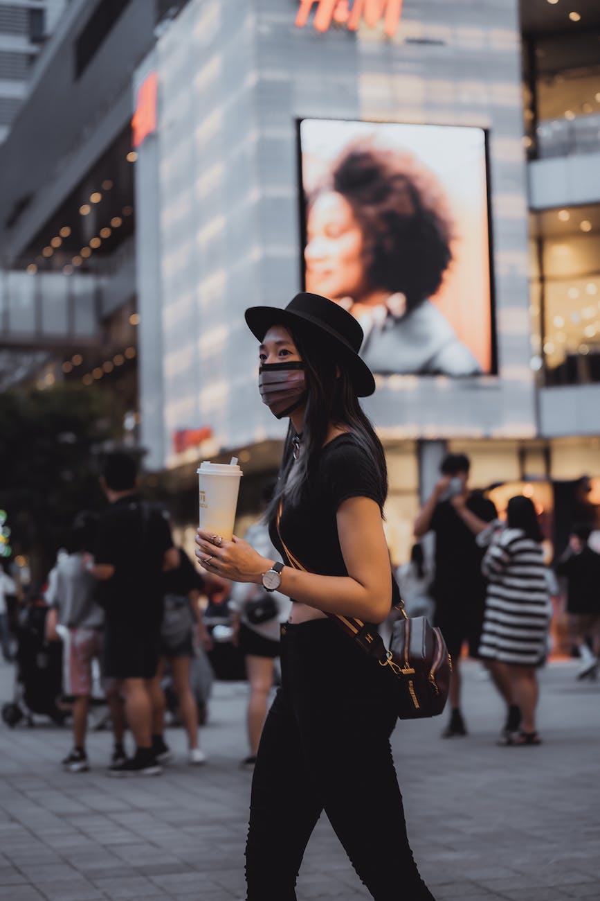 woman in a face mask walking in the city with a coffee cup