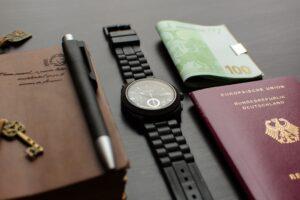 round black chronograph watch on table near germany passport an banknote on table