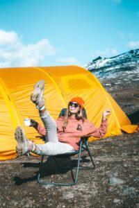 happy female sitting on chair near tent on mountain slope