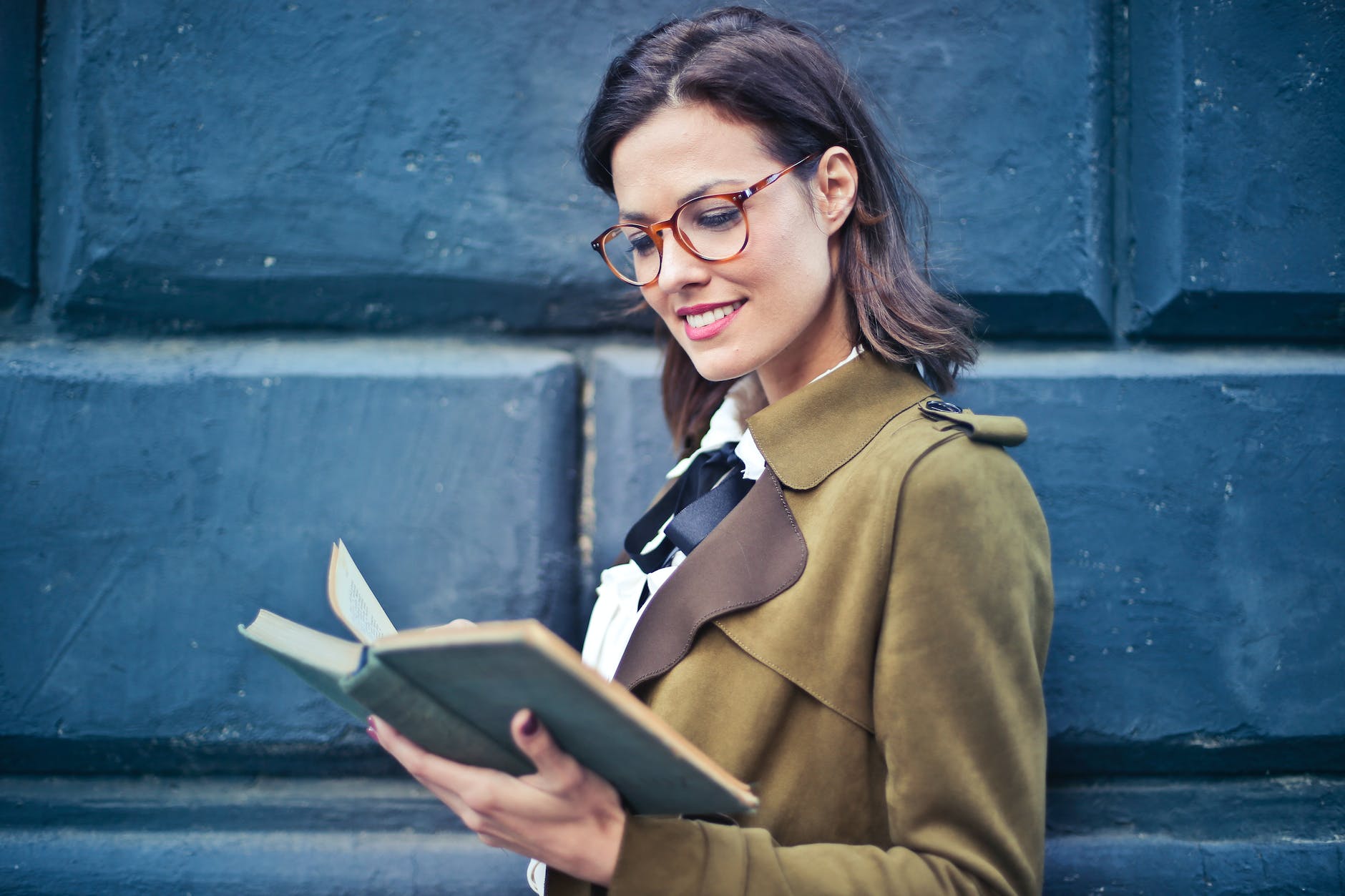woman in brown suede peacoat reading a book