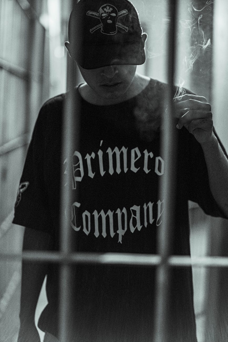 young man in black t shirt and baseball cap posing behind bars