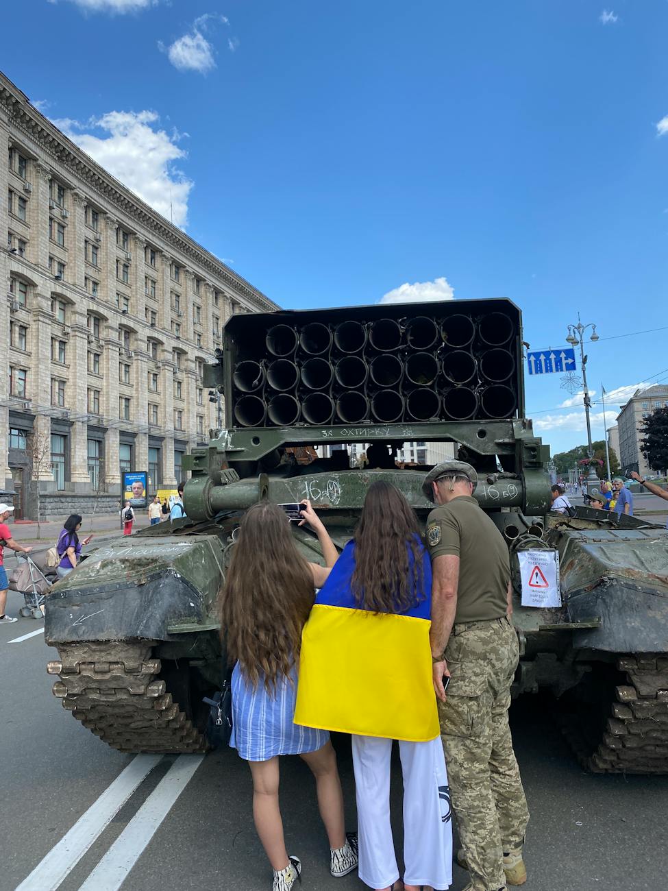 women with ukrainian flag and a soldier standing next to a tank
