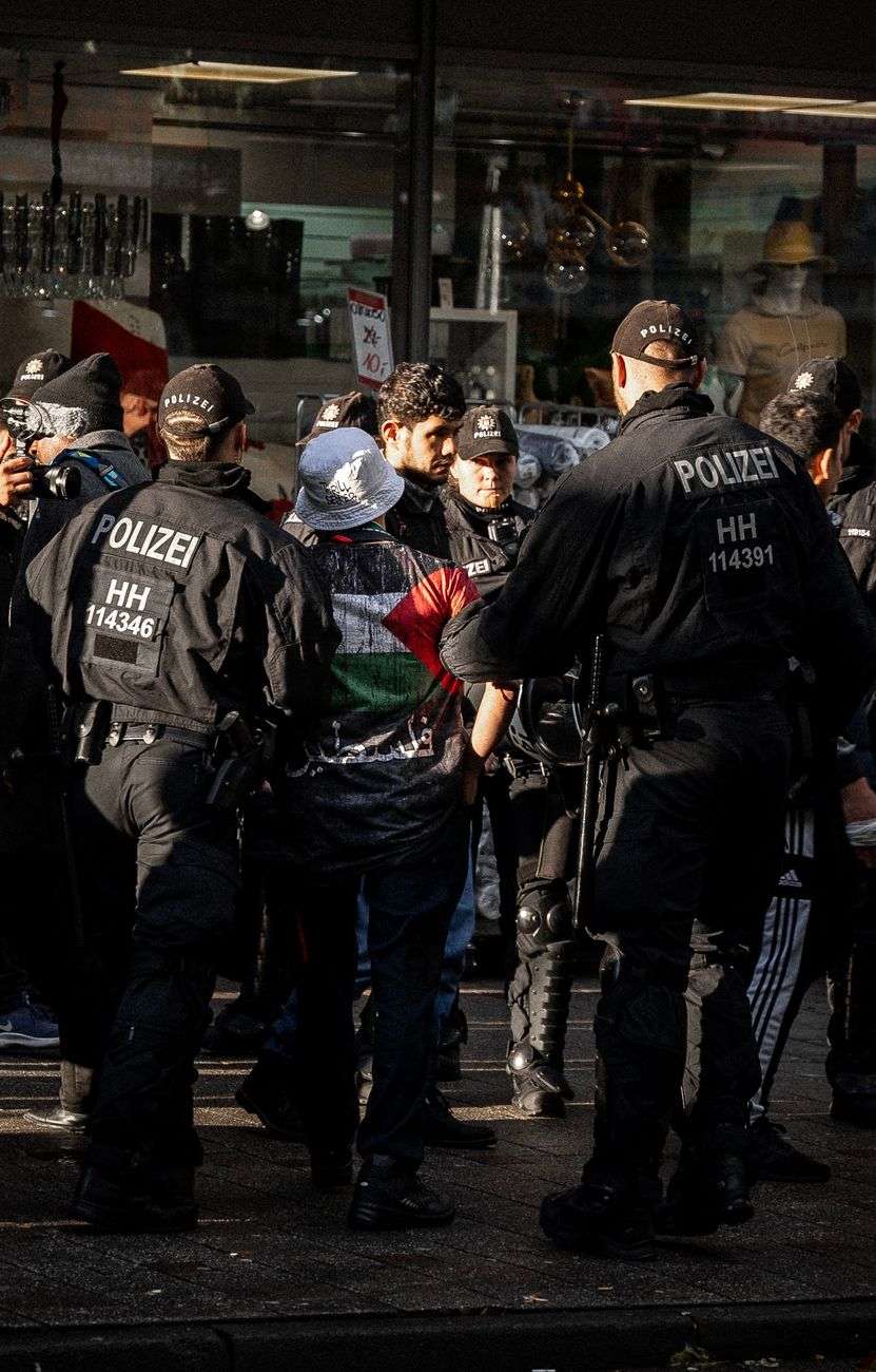 policemen holding a demonstrator wearing a t shirt with the plestine flag
