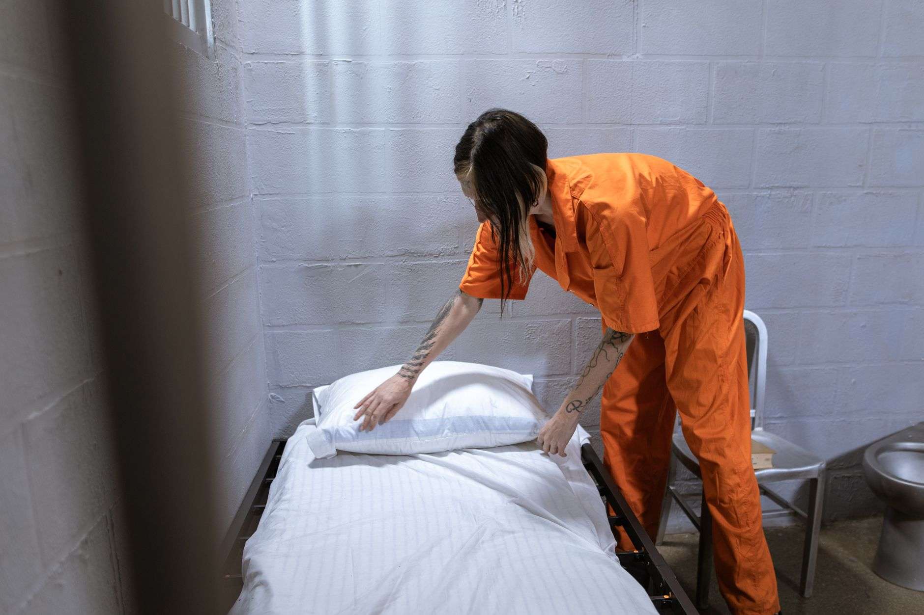 woman in orange overalls fixing bed with white linen